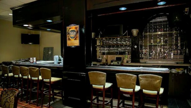 A bar area with stools, a television, and a shelf with bottles.