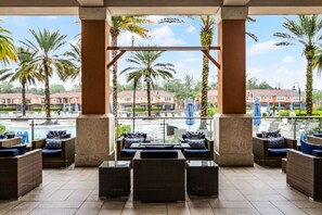A covered outdoor seating area with wicker furniture and a view of a pool and palm trees. - 2710i Lakefront 2 Master Pool Spa Disney/Universal (Kissimmee)