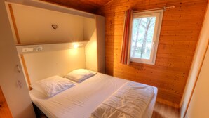 A single bed with white linens in a cabin-style room with wooden walls and a window with curtains. - Vacation Rental in Cap d'Agde: "LES PESCALUNES" (Cap d'Agde)