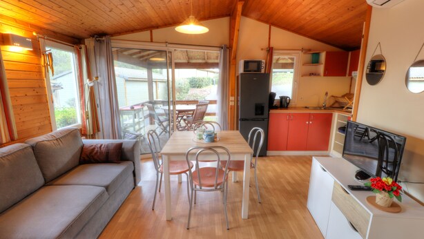 A cozy cabin interior with a sofa, dining table, chairs, a kitchen area, and a television. - Vacation Rental in Cap d'Agde: "LES PESCALUNES" (Cap d'Agde)