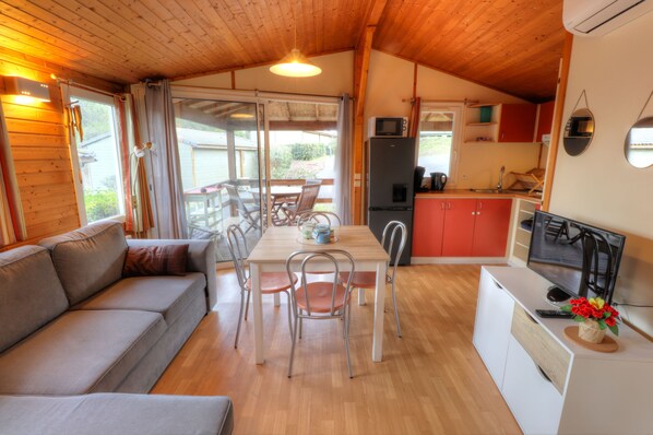 A cozy cabin interior with a sofa, dining table, chairs, a kitchen area, and a television.