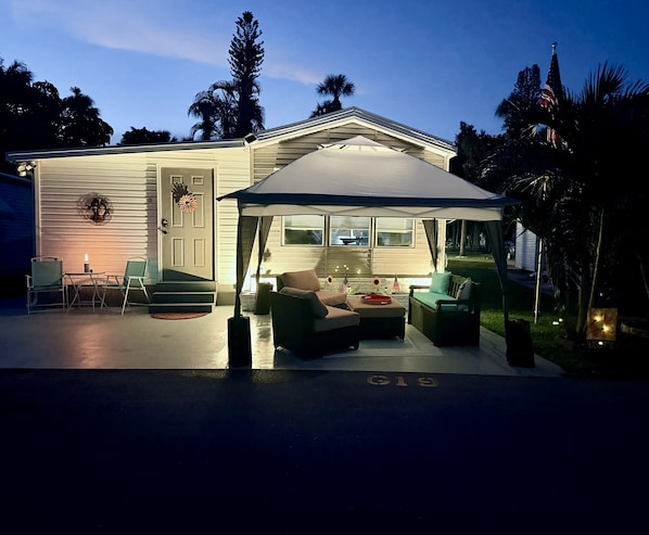 Una casa con un porche cubierto, amueblado para el exterior y una bandera.