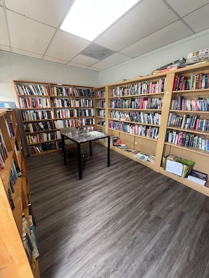 A library with wooden bookshelves, a marble table, and a ceiling with fluorescent lights.