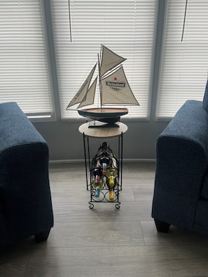 A room with a sailboat model on a table, two blue armchairs, and a wine rack with bottles.