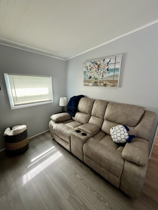 A living room with a beige sectional sofa, a lamp, a painting, a window with blinds, and a woven basket.