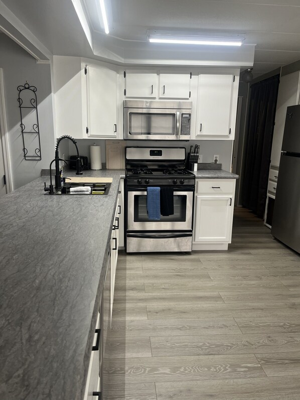 A modern kitchen with white cabinets, a built-in microwave, a stainless steel oven, and a grey countertop.