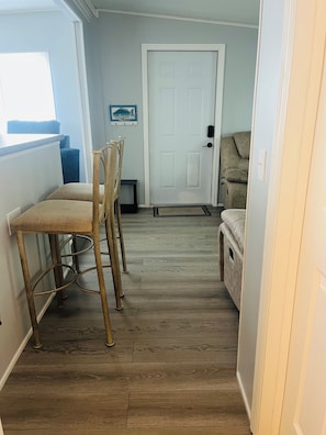 A narrow hallway with a wooden floor, a white door, and a small seating area with a couch and a chair.