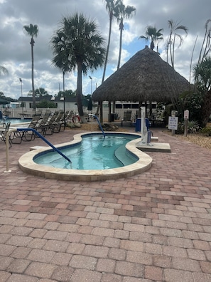 A pool area with lounge chairs, a thatched-roof structure, and palm trees.