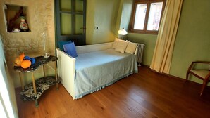 Una stanza con un letto, un tavolino con della frutta, una lampada, una sedia, una finestra con tende e una porta.