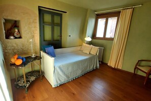 A room with a bed, a small table with fruits, a lamp, a chair, a window with curtains, and a door. - Amazing view 2-bedroom country house (Dogliani)