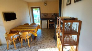 Un'area pranzo con tavolo e sedie, una cucina con lavello e utensili, e un televisore montato a parete.