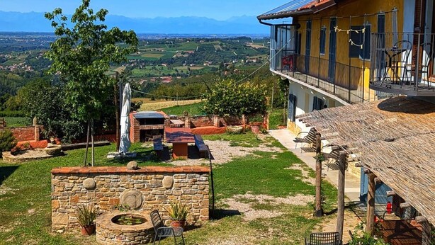 Area salotto esterna in pietra con un braciere in pietra, un tavolo e sedie, con vista su una valle panoramica e montagne sullo sfondo.