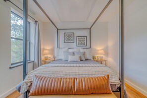 Ein Schlafzimmer mit einem Bett, zwei Nachttischen, einem Fenster und gerahmten Bildern an der Wand.