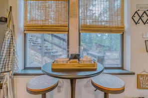 Ein Essbereich mit einem runden Tisch, zwei Hocker, einem Fenster mit Jalousien und einem Schild an der Wand.