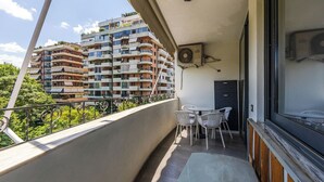 Un balcón con vistas a edificios de varios pisos, una mesa con sillas y un equipo de aire acondicionado.