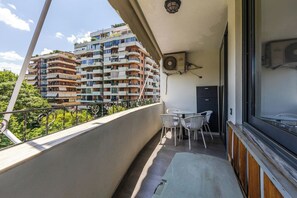 Un balcón con vistas a edificios de varios pisos, una mesa con sillas y un equipo de aire acondicionado.