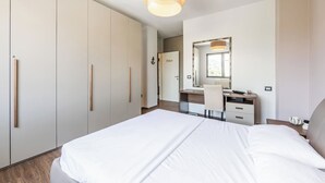 Una habitación de hotel moderna con una cama grande, un escritorio con silla, un armario y un espejo.