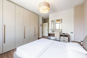 Una habitación de hotel moderna con una cama grande, un escritorio con silla, un armario y un espejo.