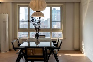 A dining area with a table and chairs, a vase with branches, and a city view through large windows. - Yidu Home -People's Square Branch (Shanghai)