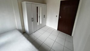 Een kamer met witte betegelde vloer, een garderobe met meerdere deuren, en een donkerhouten deur.