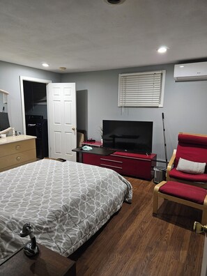 Ein Schlafzimmer mit einem Bett, einem Fernseher, einem roten Sessel, einem Schminktisch und einer Tür zu einem Badezimmer.