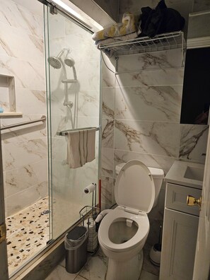 Ein Badezimmer mit Duschkabine, Toilette, Mülleimer und Waschbecken.