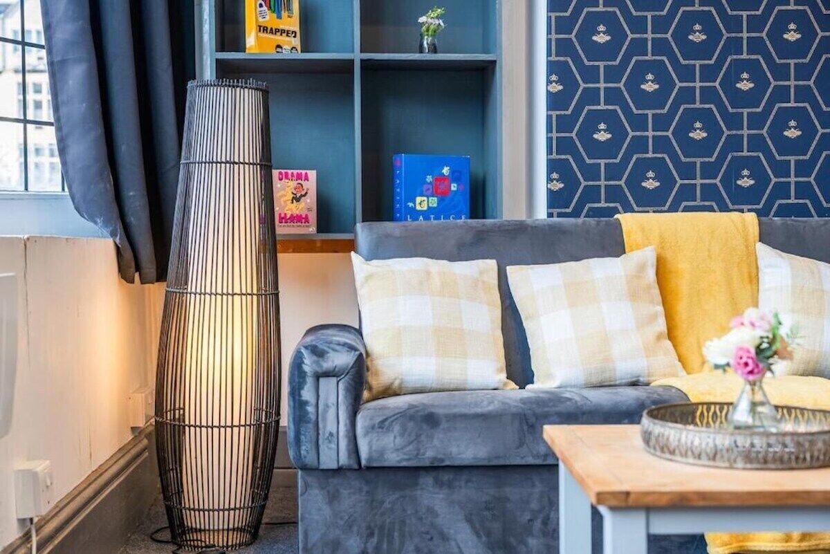 A living room with a grey sofa, a tall floor lamp, and a bookshelf with books and decorative items.