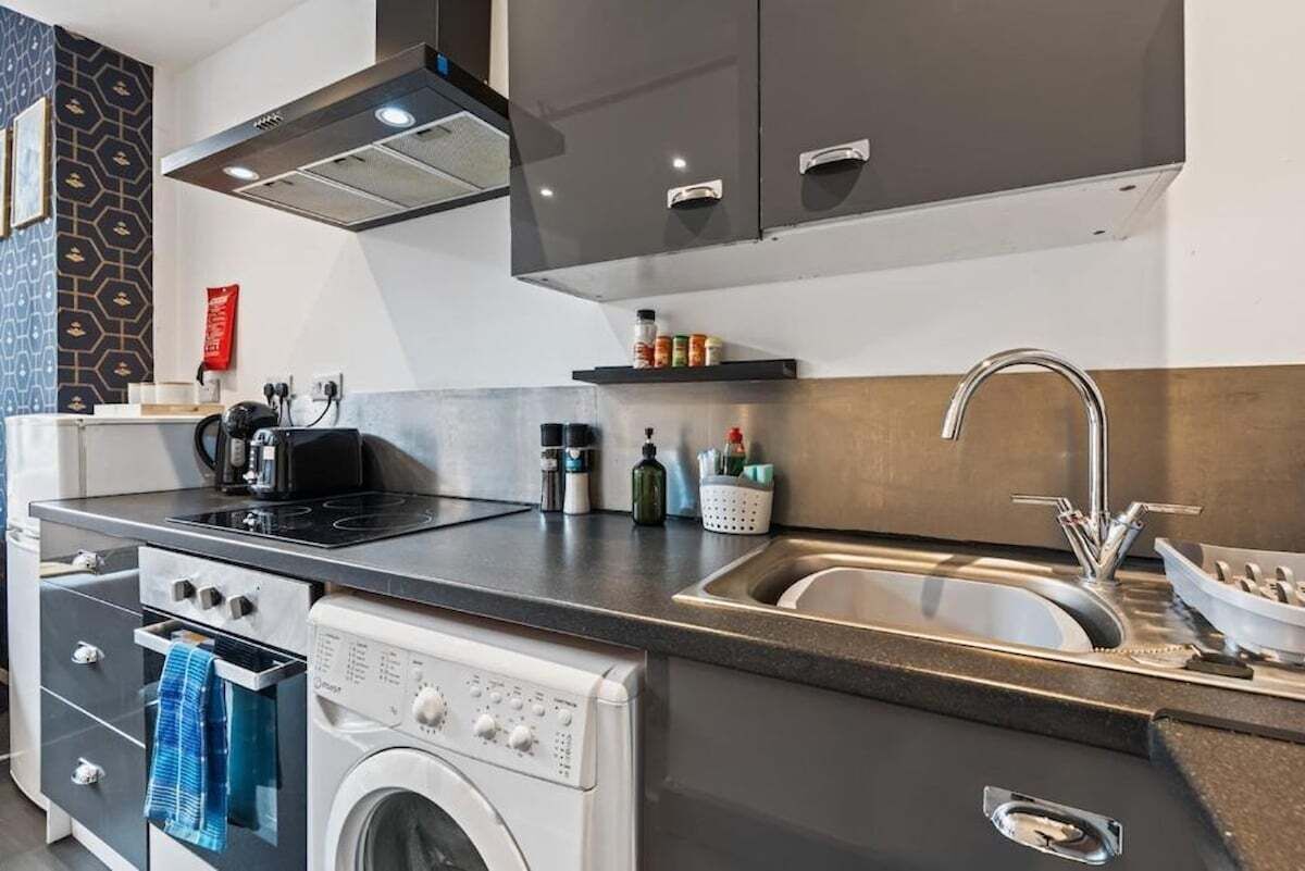 Une cuisine moderne équipée d’un lave-linge et d’un sèche-linge intégrés, d’un évier en acier inoxydable et d’un plan de travail noir.