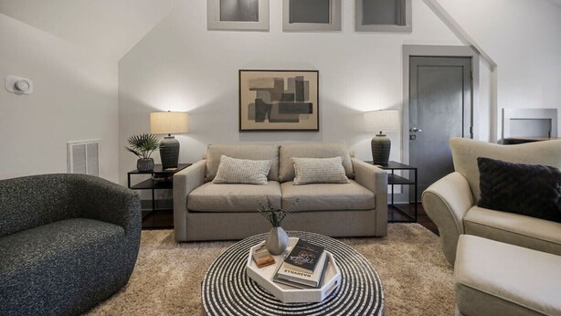 Ein modernes Wohnzimmer mit einem grauen Sofa, einem runden Couchtisch mit Büchern, einem grauen Sessel und einem Gemälde an der Wand.