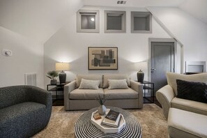 Uma sala de estar moderna com um sofá cinzento, uma mesa de centro redonda com livros, uma poltrona cinzenta e um quadro na parede.