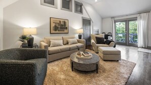 Ein modernes Wohnzimmer mit einer Couch, einem Sessel, einem Hocker, einem Couchtisch und einem Deckenventilator.