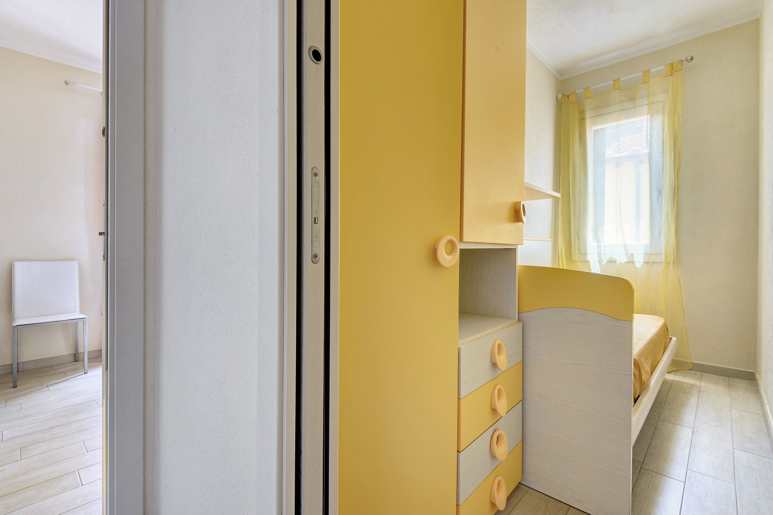 Una stanza arredata con un letto, una sedia, un armadio e una finestra con tende.