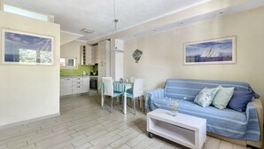 A modern living room with a sofa, dining table, chairs, and a kitchen in the background.