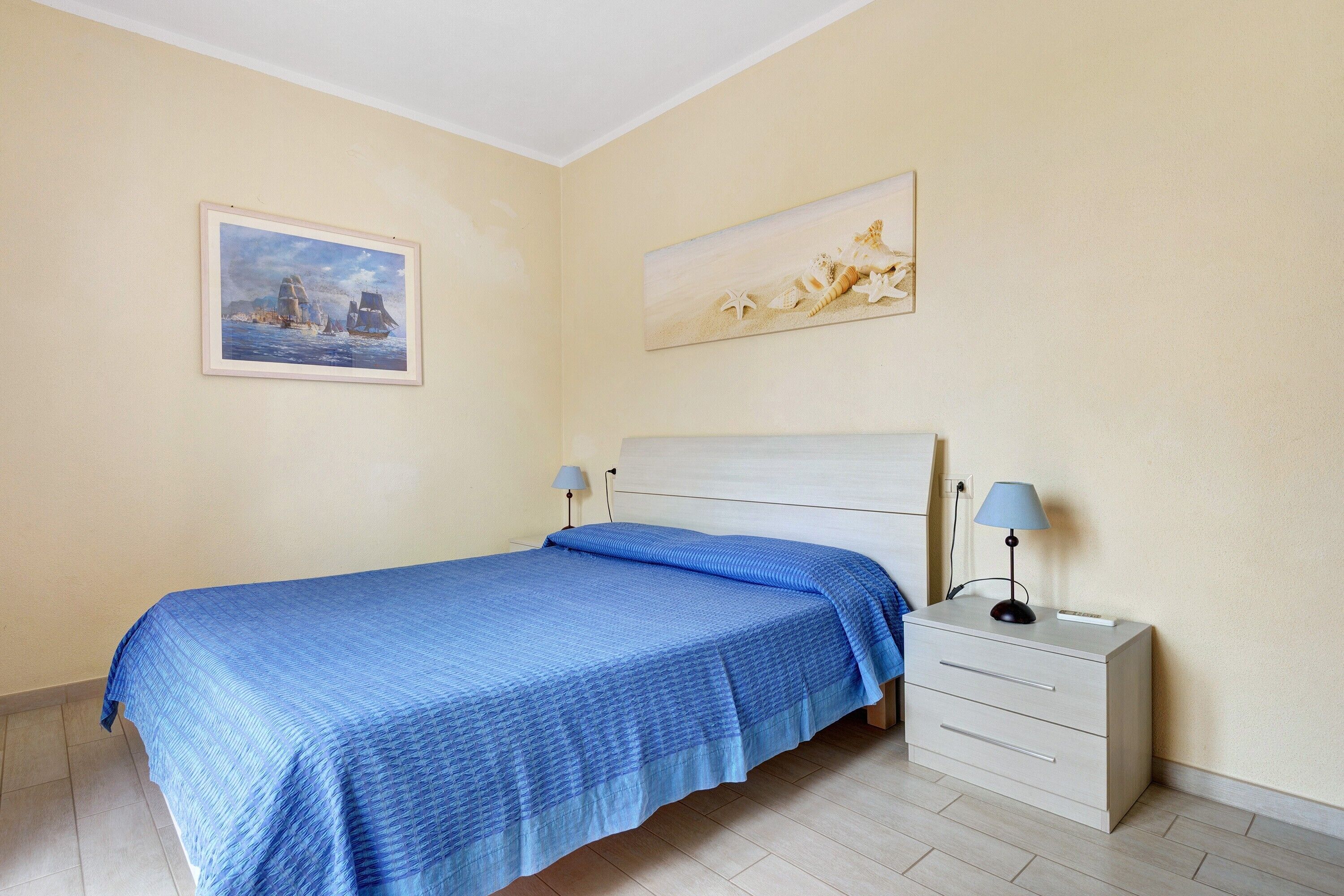 A bedroom with a bed, a nightstand, a lamp, and two paintings on the wall.