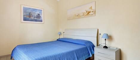 A bedroom with a bed, a nightstand, a lamp, and two paintings on the wall.