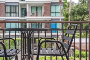 Ein Balkon mit Tisch und zwei Stühlen, einem Geländer und einem Gebäude mit mehreren Fenstern im Hintergrund.