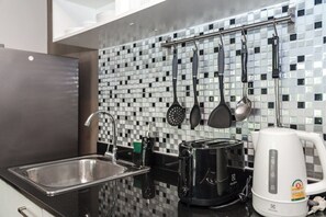 Eine Küche mit Spüle aus Edelstahl, einem schwarzen Toaster, einem weißen Wasserkocher und einer Spritzschutzwand mit Mosaikfliesen.