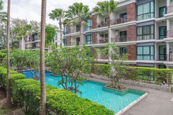 Ein mehrstöckiges Hotel mit Swimmingpool, umgeben von üppiger Vegetation und Palmen.