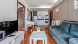 Een moderne woonkamer met een flatscreen televisie, een bank, een salontafel en een keuken op de achtergrond.