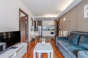 Ein modernes Wohnzimmer mit Flachbildfernseher, einer Couch, einem Couchtisch und einer Küche im Hintergrund.