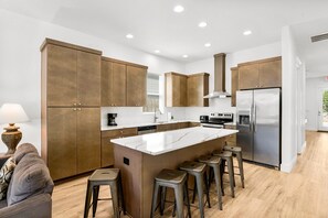 Eine moderne Küche mit Holzausstattung, einer zentralen Kochinsel mit Barhocker und Edelstahlgeräten.