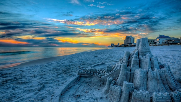 Une plage avec un grand château de sable en premier plan.