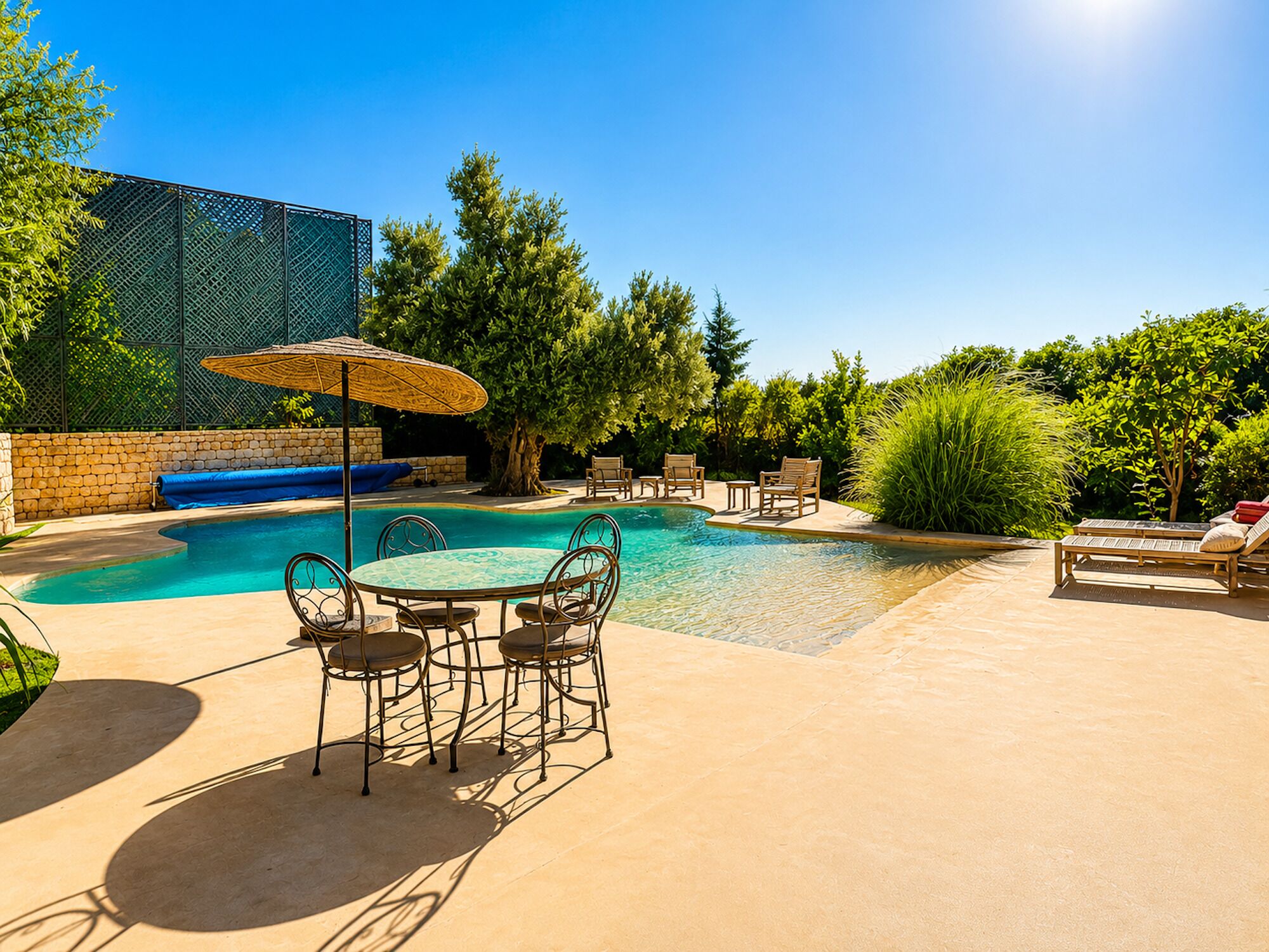 Una piscina con un muro de piedra, una mesa cubierta con sillas y sillones de descanso.