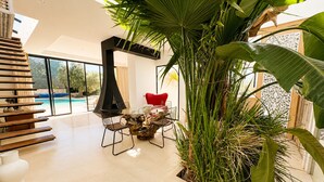 A modern interior with a glass table, chairs, a red chair, and a large plant. - Palais Pleya (Essaouira)
