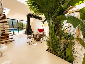 A modern interior with a glass table, chairs, a red chair, and a large plant. - Palais Pleya (Essaouira)