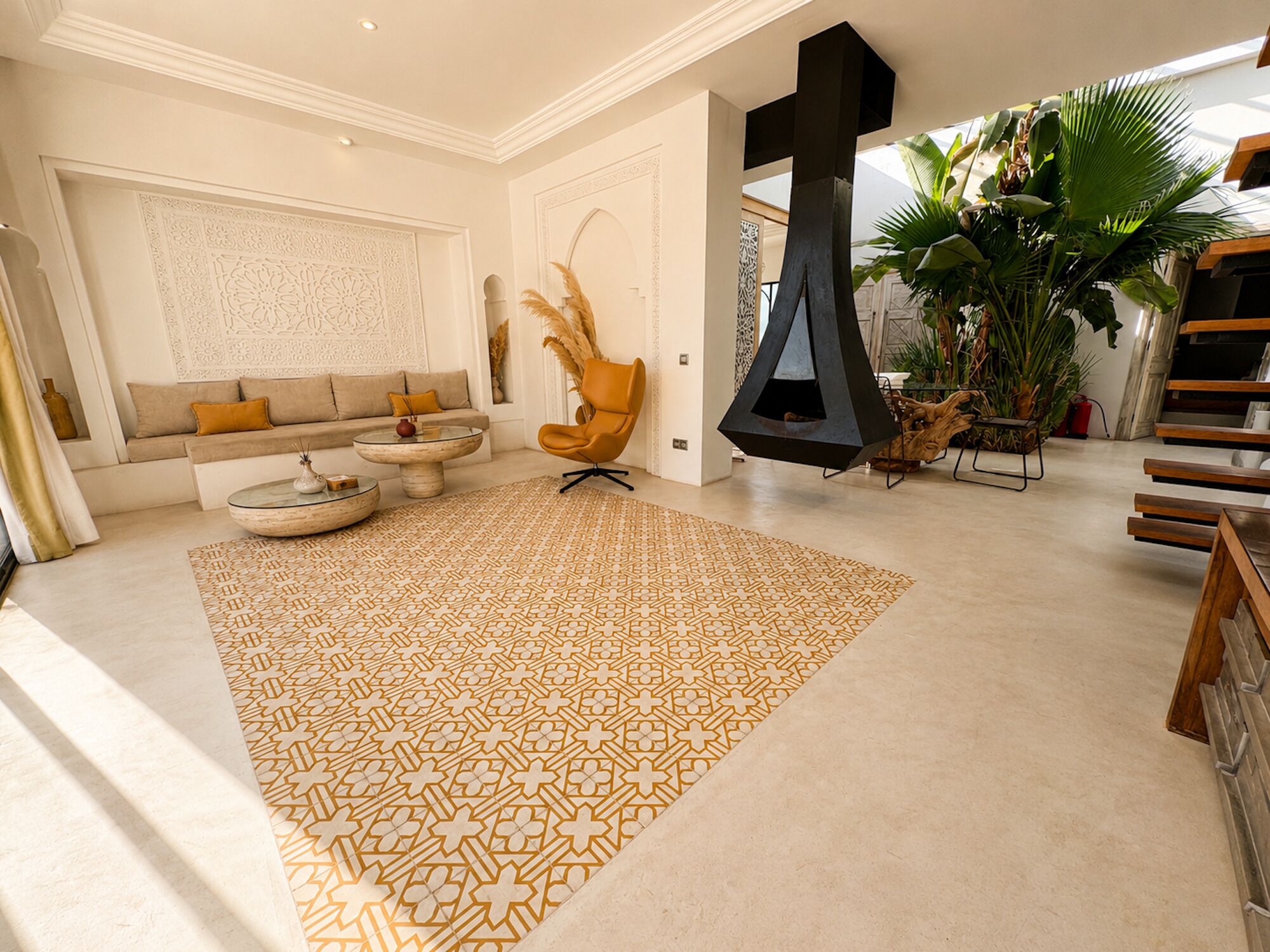 Un salón espacioso con un gran tapiz estampado, un sofá con cojines, una mesa de centro, un sillón colgante y una planta de gran tamaño.