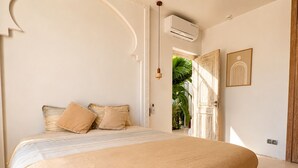 A bedroom with a bed, pillows, an air conditioning unit, a door, and a wall-mounted light fixture. - Palais Pleya (Essaouira)