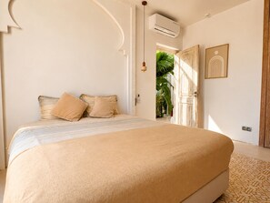 A bedroom with a bed, pillows, an air conditioning unit, a door, and a wall-mounted light fixture. - Palais Pleya (Essaouira)