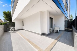 A modern building with a flat roof, a covered outdoor area with a table and chairs, and a small garden area. - GuestHost - Perla Nera Apartment 3 near the sea (Trani)