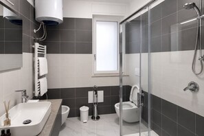 A modern bathroom with a bathtub, toilet, bidet, and glass shower enclosure. - GuestHost - Perla Nera Apartment 3 near the sea (Trani)